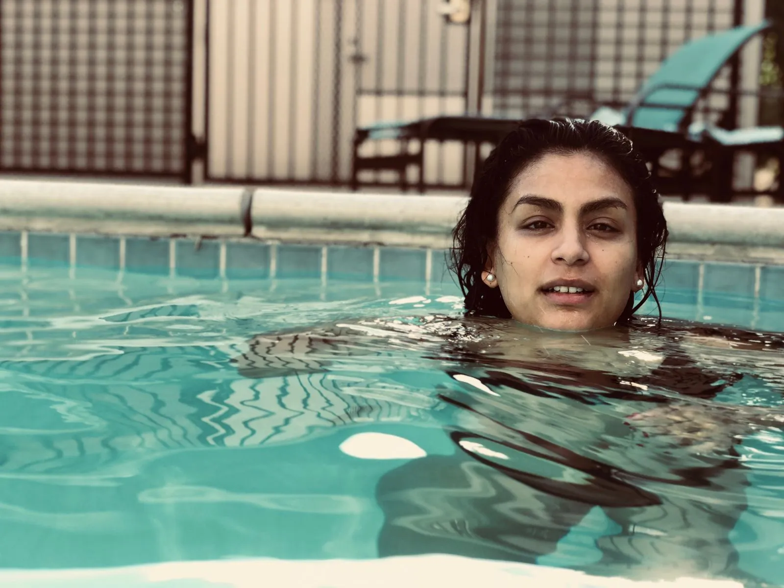 A woman enjoys a refreshing swim in a pool during a sunny summer day, outdoors.